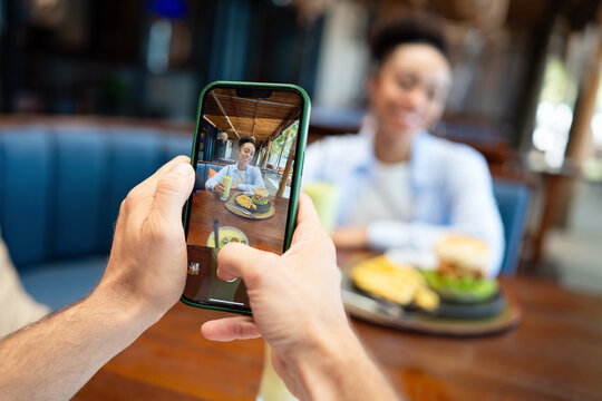 Diverse couple goes photo first in mobile dining, capturing a moment with smartphone, social ritual