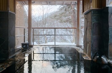 Winter scene of a public hot spring bath in a traditional Japanese Onsen Ryokan, with a view of withered trees on the snowy hillside in an atmosphere of Wabi Sabi beauty, in Takayama, Nagano, Japan