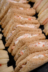 Row of brown bread sandwiches on a black catering platter