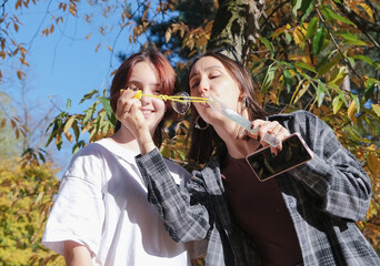 mother with her daughter walking in autumn park blowing soap bubbles