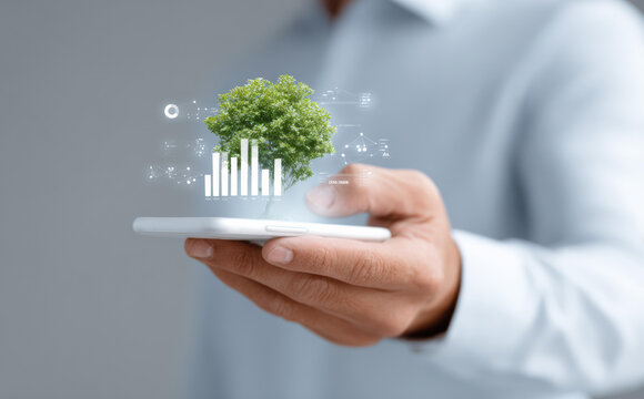 Professional businessman hand holding smartphone with futuristic hologram of green tree and graph, representing financial growth and investment in sustainable technology