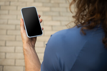 Young brunette caucasian man wearing blue t-shirt used mobile phone. Check apps, focused on device, chatting or browsing internet. Outdoors. Back view.