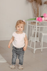 Cute toddler in casual outfit stands confidently in a bright, simple room with flowers on a table