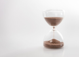 Hourglass with sand running on gray background. Concept for time management, deadline, urgency, or countdown. Sandglass half empty with falling sand kernels. Symbol of passing time. Selective focus.