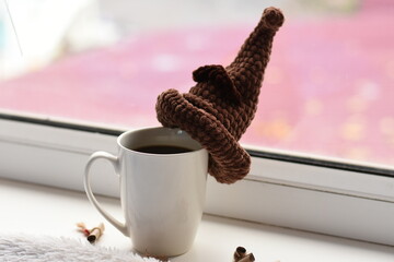Side view of coffee cup on windowsill with small knitted brown hat, gray blanket, rolled notes and...