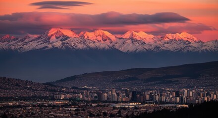 Dramatic sunset over snow-capped mountain range and urban cityscape