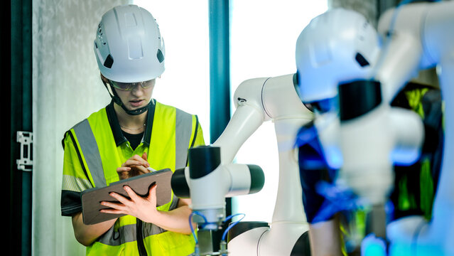 Two female robotics engineers in an R and D lab program an artificial intelligence cobot. They use a tablet to test the robot's motion control and sensor vision with blocks.