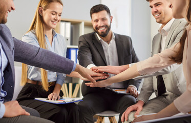 Happy smiling young business people company employees in formal clothes putting their arms together...