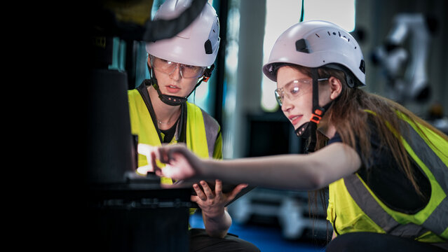 Two female robotics engineers in an R and D lab troubleshoot an artificial intelligence cobot. They are inspecting the robotic system hardware and programming.