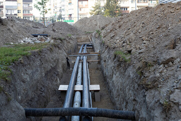 Construction work involves laying pipes in a trench within an urban area during daylight hours