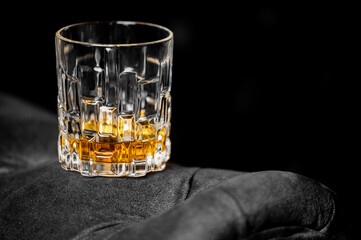 A crystal whiskey tumbler with a geometric pattern, filled with amber liquor on a black background, with copy space