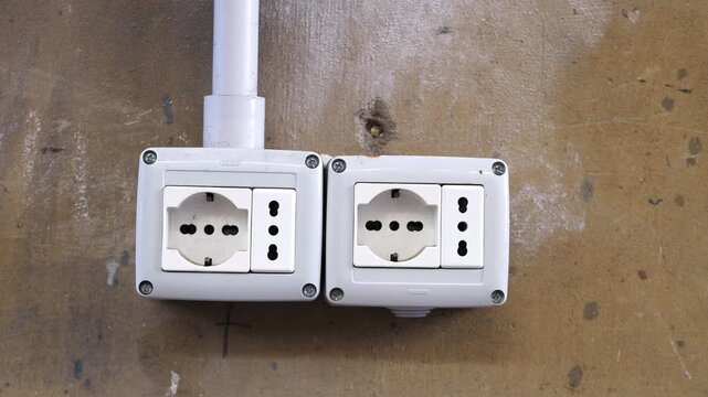A close look at a hand inserting a power plug into a weathered wall socket, highlighting everyday gestures in an urban environment.