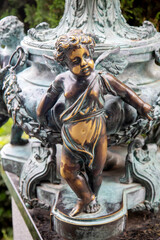 A bronze boy figurine with a polished tummy on a bright sunny day. Flora, nature, plants, landscape...