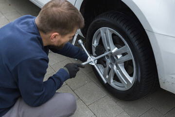 Young man unscrewing lug nuts on a car wheel with a wrench while replacing a flat tire on the road