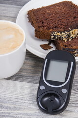 Glucometer for measuring sugar level, sweet chocolate cake and cup of coffee with milk. Nutrition during diabetes