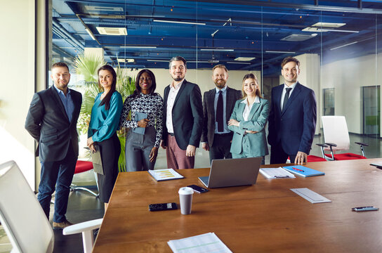 Fototapeta Portrait of friendly multiracial team of business professionals standing together in a row in conference room. Cheerful diverse male and female managers crew looking at camera in different poses.