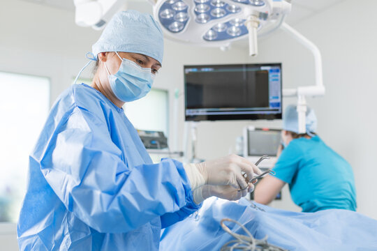 Surgeon in blue scrubs and mask focuses on a procedure while a nurse assists in a well-lit surgical room. - Powered by Adobe
