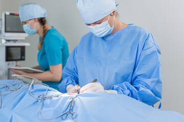 Surgeons in blue scrubs conduct a delicate surgical procedure in a bright operating room, focused on their task.