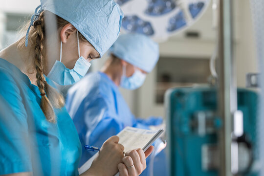 Surgical team reviews patient data in blue scrubs while preparing equipment in an operating room setting.