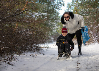 Little boy with his mother on a sledding hill in the forest during winter.