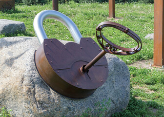 A large rusty metal padlock with a decorative key on a stone outside