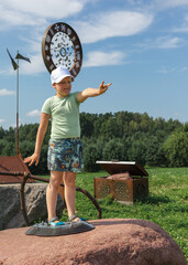 A little boy climbing a mountain and standing on a large rock poses and shows a his victory