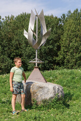 A little boy stands near a stone and looks at the wind sculpture