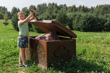 A little boy opens a large metal chest and finds a large stone inside