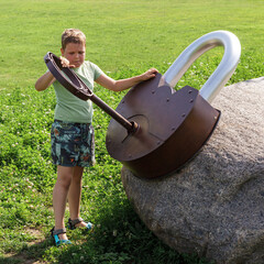 A little boy on the playground is trying hard to unlock a giant lock with a large metal key. Square photo