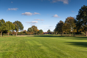 Golf course fairway with clubhouse and autumn trees under blue sky