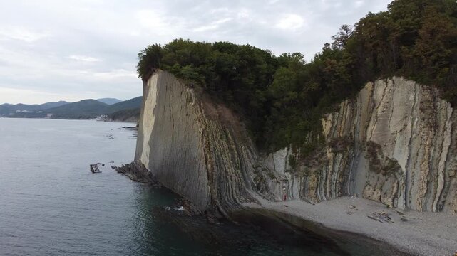 Drone footage flying diagonally away from Kiseleva Rock cliff into open sea under cloudy sky