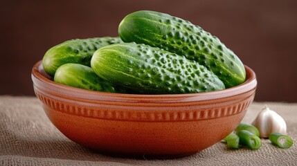 Sour pickles in a ceramic bowl surrounded by fresh green onions and garlic on a rustic tablecloth