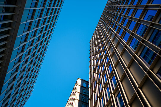 Modern city architecture seen upward with intersecting structure and facade geometry creating symmetry and dynamic perspective under the bright skyline of an urban environment