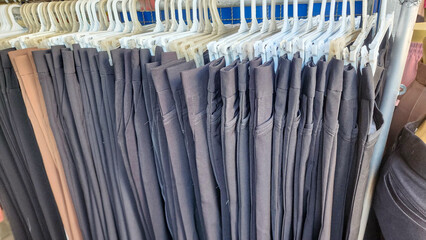 a clothing rack with several pairs of pants hanging on white plastic hangers. Most of the pants are dark-colored—mainly black or dark blue.The pants are neatly arranged and folded over the hangers.