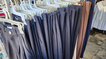 a clothing rack with several pairs of pants hanging on white plastic hangers. Most of the pants are dark-colored—mainly black or dark blue.The pants are neatly arranged and folded over the hangers.