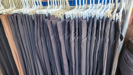 a clothing rack with several pairs of pants hanging on white plastic hangers. Most of the pants are dark-colored—mainly black or dark blue.The pants are neatly arranged and folded over the hangers.