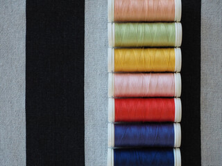 Top view of multicolored sewing threads on striped textile surface for fashion design and craft