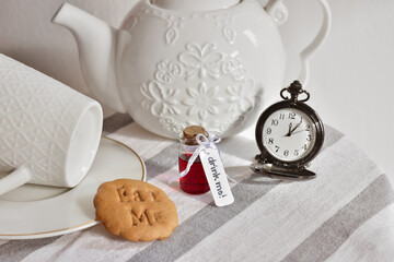 ''Eat me'' cookie and ''Drink me'' potion on the table next to a pocket watch and a teapot