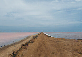 A dirt road separates the pink lake from the salt lake - A unique landscape of colorful salt flats in Cumaraguas, Venezuela, under a cloudy sky 