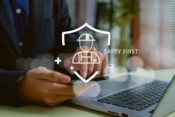 professional using a smartphone and laptop to manage workplace safety digitally. Virtual safety first icon with helmet and shield representing protection, risk control, and smart safety management.