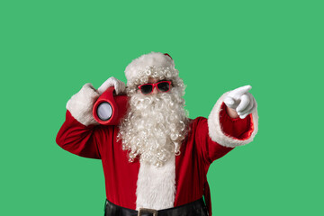 Santa Claus with a white curly beard, wearing a red suit and sunglasses, dances cheerfully with a portable speaker on a green background. Perfect for Christmas themed compositions.