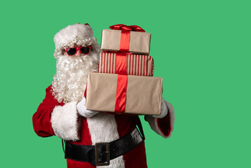 Santa Claus with a white curly beard, wearing a red suit and sunglasses, peeks out from behind boxes of gifts on a green background. Ideal for Christmas themed compositions and holiday layouts.