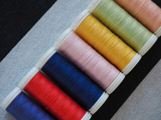 Set of bright sewing threads in rainbow colors on black and white striped fabric background