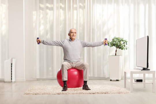 Elderly man exercising with small weights and sitting on a fitness ball - Powered by Adobe