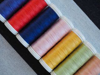 Vibrant sewing thread spools arranged in a row on black and white striped fabric background
