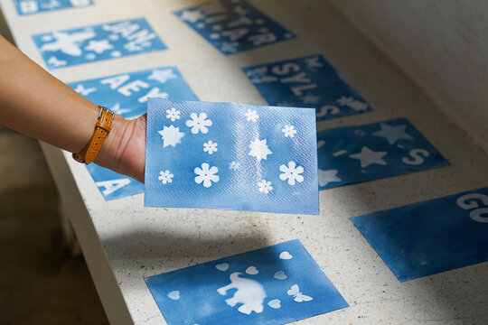 Hand holding a unique blue cyanotype card with flower and star stencil patterns. Sun printing, handmade craft, and artistic concept.