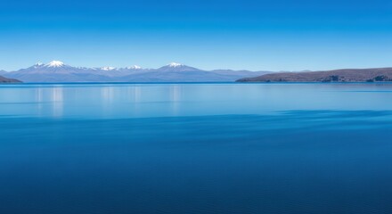 Fototapeta premium Tranquil blue lake with snow-capped mountain view under clear sky