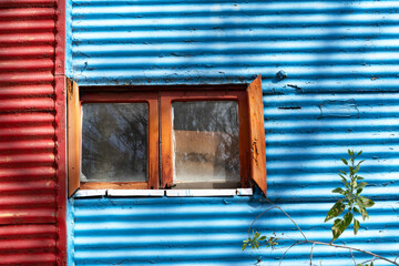 Small wooden and glass window in the middle of the tiled wall of a colorful building in La Boca, Buenos Aires
