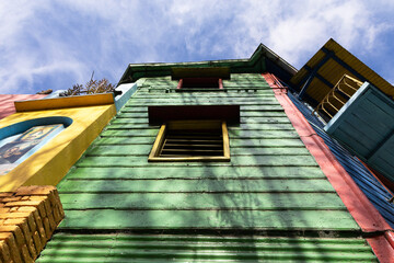 Tall building with colorful walls made of various materials, such as tile, brick, and wood, photographed from below showing the blue sky