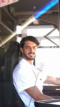 Handsome male bus driver with a beard smiling at the camera while driving a public transport vehicle during his daily city route in slow motion